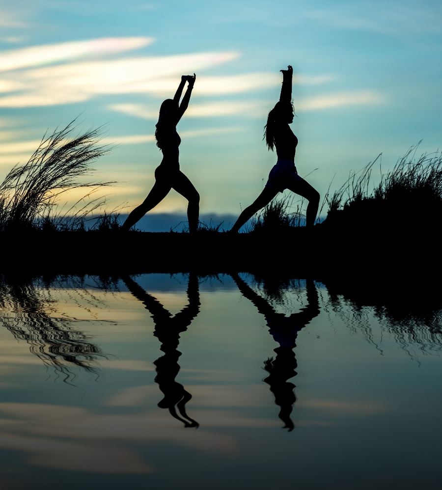 Two people doing yoga by the water at sunset